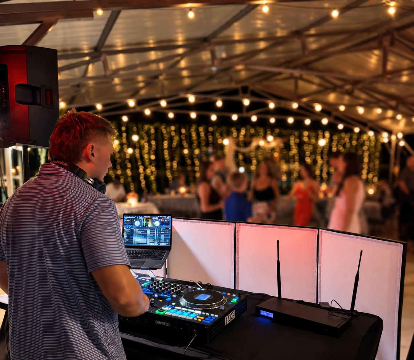 DJ Crim at the decks during a tented wedding reception, with guests dancing under string lights